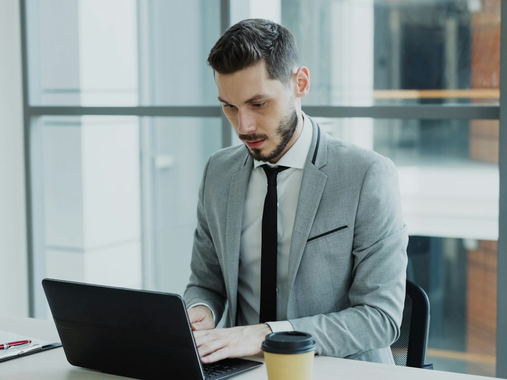 Un professionnel en costume, concentré devant son ordinateur portable, dans un bureau lumineux.