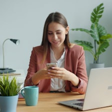 Une indépendante consulte son téléphone à son bureau, ordinateur ouvert.