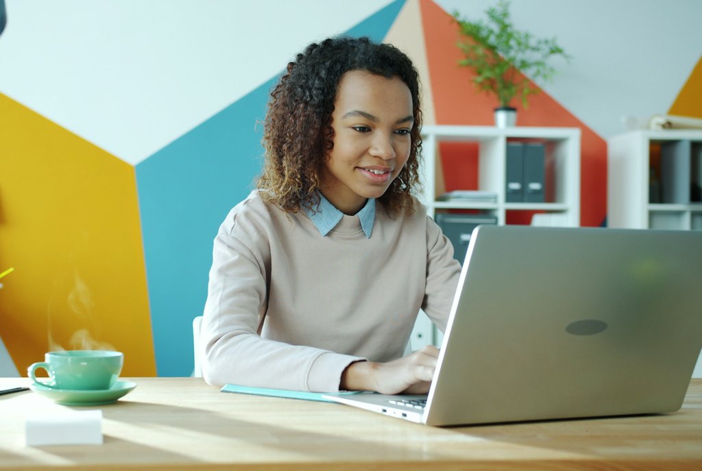 Une femme sourit en consultant son ordinateur portable à son bureau.